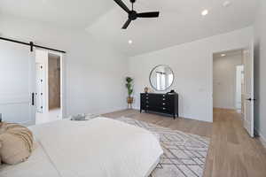 Bedroom featuring a barn door, vaulted ceiling, light wood-style flooring, recessed lighting, and ceiling fan