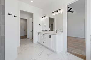 Bathroom with double vanity, baseboards, marble look tiles, and recessed lighting
