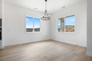 Spare room with a chandelier, plenty of natural light, light wood-style flooring, and baseboards