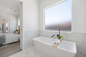 Bathroom with healthy amount of natural light, a freestanding bath, tile walls, marble finish flooring, and ensuite bathroom