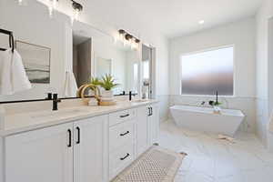 Full bathroom with double vanity, a soaking tub, marble finish flooring, wainscoting, and recessed lighting