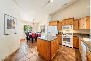 Kitchen featuring white appliances, a kitchen island, baseboards, decorative light fixtures, and dark stone counters