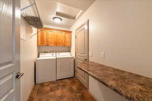 Washroom with cabinet space, washer and dryer, a textured ceiling, dark stone finish flooring, and baseboards