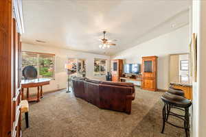Carpeted living room featuring vaulted ceiling, a ceiling fan, and baseboards