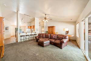 Living room featuring light colored carpet, vaulted ceiling, a ceiling fan, baseboards, and a textured ceiling