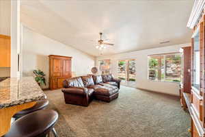 Living area featuring light carpet, a ceiling fan, vaulted ceiling, a textured ceiling, and baseboards