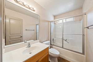 Bathroom with toilet, vanity, and bath / shower combo with glass door