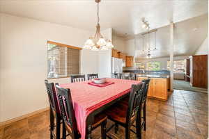 Dining space featuring a chandelier, vaulted ceiling, baseboards, ceiling fan, and stone tile floors