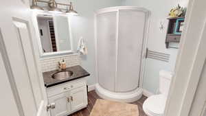 Bathroom with a stall shower, toilet, vanity, wood finished floors, and decorative backsplash