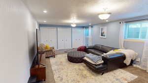 Carpeted living area with healthy amount of natural light, baseboards, a textured ceiling, and recessed lighting