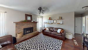 Living area featuring ceiling fan, wood finished floors, a brick fireplace, and baseboards