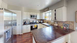 Kitchen with appliances with stainless steel finishes, a sink, dark countertops, a peninsula, and dark wood finished floors