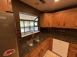 Kitchen featuring white dishwasher, a sink, lofted ceiling, and brown cabinetry