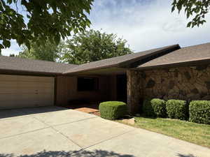View of front facade with concrete driveway, an attached garage, a shingled roof, and brick siding