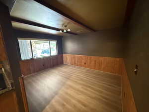Unfurnished room featuring wood walls, wainscoting, wood finished floors, beamed ceiling, and a fireplace