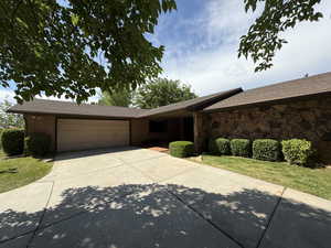 Single story home with an attached garage, driveway, and brick siding