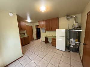 Kitchen featuring freestanding refrigerator, gas water heater, light tile patterned flooring, brown cabinets, and light countertops