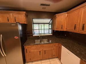 Kitchen featuring freestanding refrigerator, a sink, dishwasher, light tile patterned flooring, and brown cabinetry