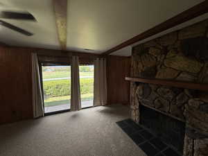 Unfurnished living room featuring beamed ceiling, wood walls, carpet, and a fireplace