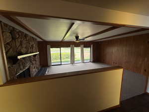 Unfurnished living room featuring wood walls, a ceiling fan, a fireplace, and beam ceiling