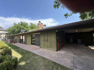 Back of property with board and batten siding, a chimney, a patio, and a lawn