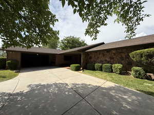 Ranch-style house with concrete driveway, an attached garage, stone siding, a front lawn, and brick siding