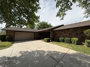 Ranch-style house with a garage, driveway, brick siding, and a shingled roof