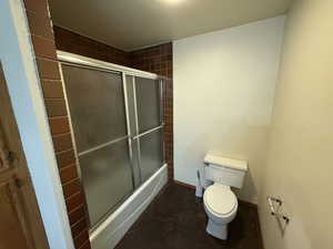 Full bath with toilet, bath / shower combo with glass door, and baseboards