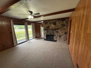 Unfurnished living room featuring beamed ceiling, wood walls, carpet, a ceiling fan, and plenty of natural light