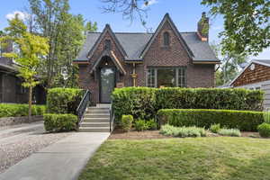 English style home featuring brick siding, a chimney, and a front lawn