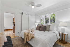 Bedroom with wood finished floors, crown molding, baseboards, a barn door, and ceiling fan