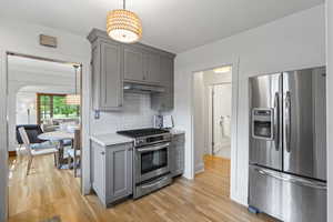 Kitchen featuring stainless steel appliances, gray cabinets, under cabinet range hood, light countertops, and light wood-style floors