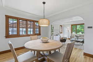 Dining room featuring arched walkways, baseboards, light wood-type flooring, a fireplace, and ornamental molding