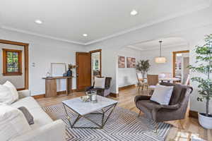 Living area with arched walkways, light wood-type flooring, baseboards, recessed lighting, and crown molding