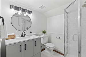 Full bath with toilet, vanity, a shower stall, vaulted ceiling, and wainscoting