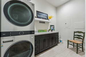 Washroom with stacked washer / drying machine, electric panel, light tile patterned flooring, cabinet space, and baseboards