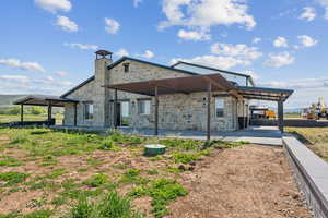 Rear view of house featuring stone siding, a patio, and a chimney
