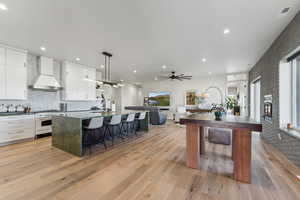 Kitchen with premium range hood, a kitchen island with sink, a breakfast bar, white cabinetry, and light wood-style flooring