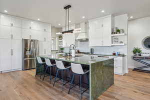Kitchen with stainless steel fridge, open shelves, wall chimney range hood, a sink, and backsplash