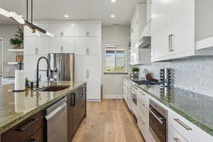 Kitchen featuring stainless steel appliances, a sink, recessed lighting, light wood-style flooring, and light stone counters