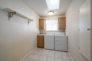 Laundry room featuring independent washer and dryer, baseboards, cabinet space, light tile patterned floors, and a skylight