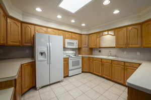 Kitchen with white appliances, a sink, crown molding, brown cabinetry, and light countertops