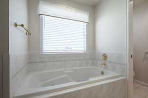 Bathroom with toilet, a jetted tub, and tile patterned flooring