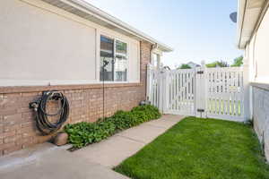 View of side of home with a gate, brick siding, and stucco siding