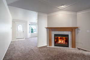 Carpeted foyer featuring a fireplace, ornamental molding, and baseboards