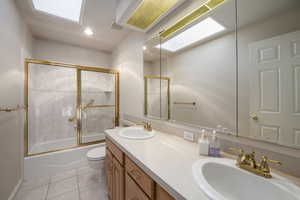 Bathroom with double vanity, toilet, shower / bath combination with glass door, tile patterned floors, and recessed lighting