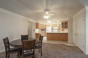 Dining room with light colored carpet, a raised ceiling, a ceiling fan, crown molding, and light tile patterned flooring