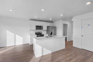 Kitchen featuring stainless steel appliances, a sink, white cabinets, an island with sink, and baseboards