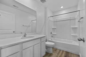 Bathroom with toilet, vanity, shower / bath combination, and wood finished floors