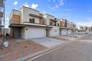 View of front facade featuring stucco siding, a residential view, a garage, driveway, and central air condition unit